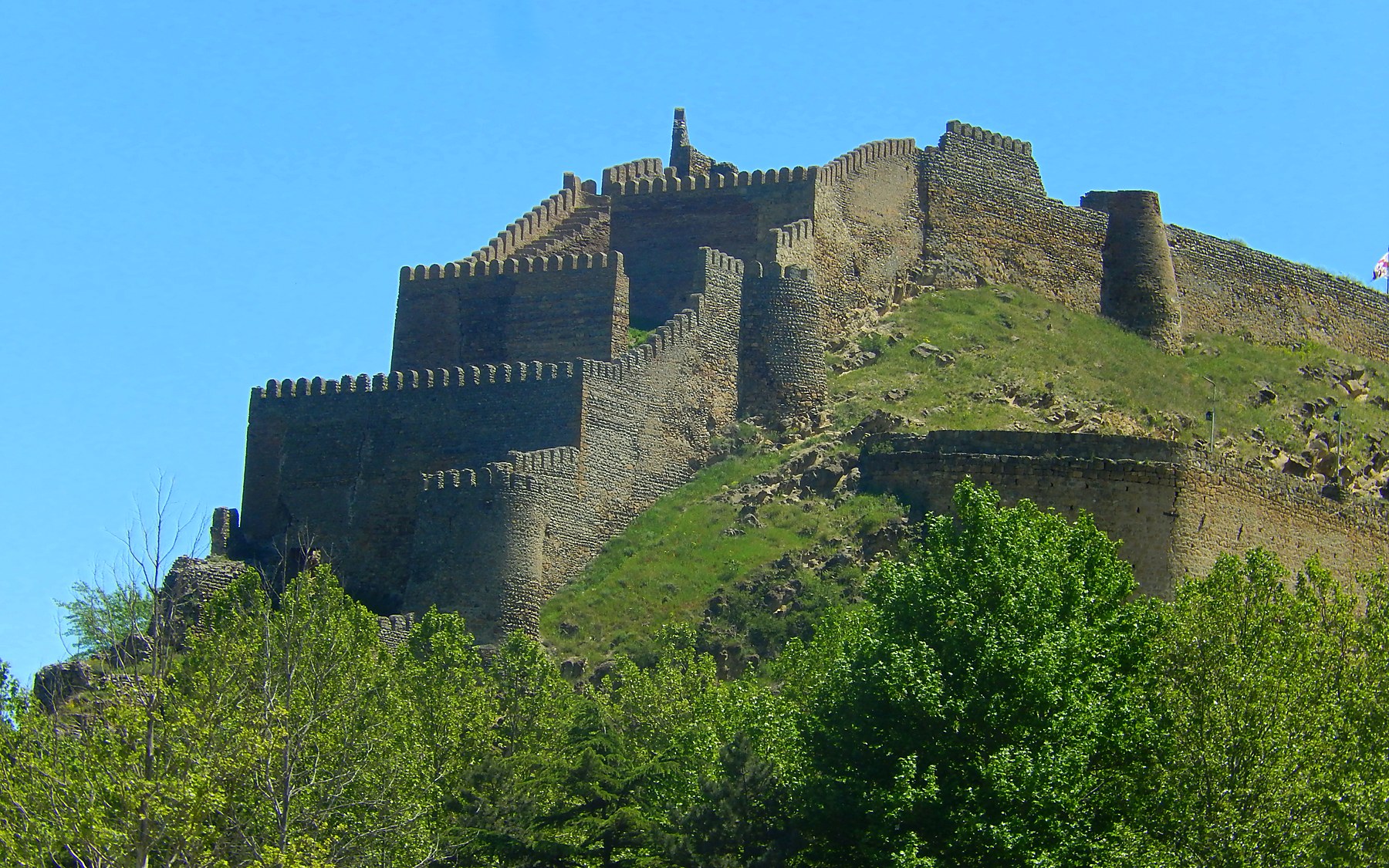 Stone fortress walls on a green hillside in Gori