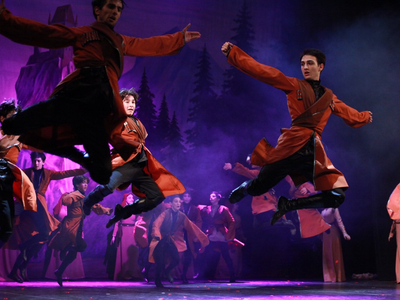 Georgian folk dancers leaping on stage in traditional chokha costumes
