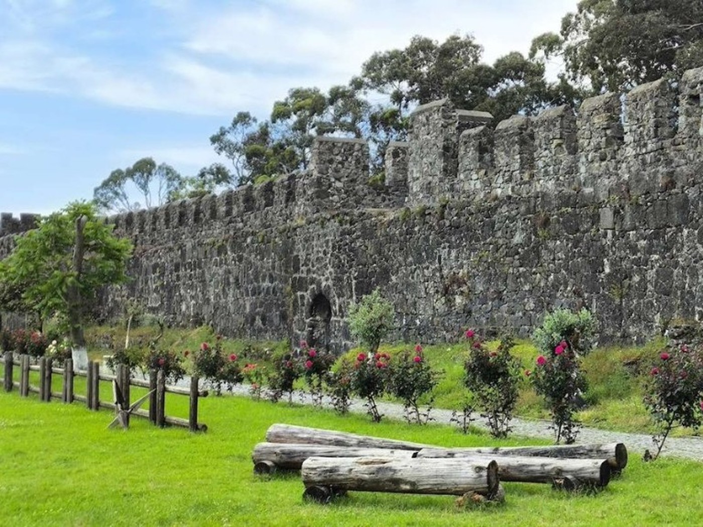Stone walls of Gonio fortress with roses and a green lawn under a blue sky