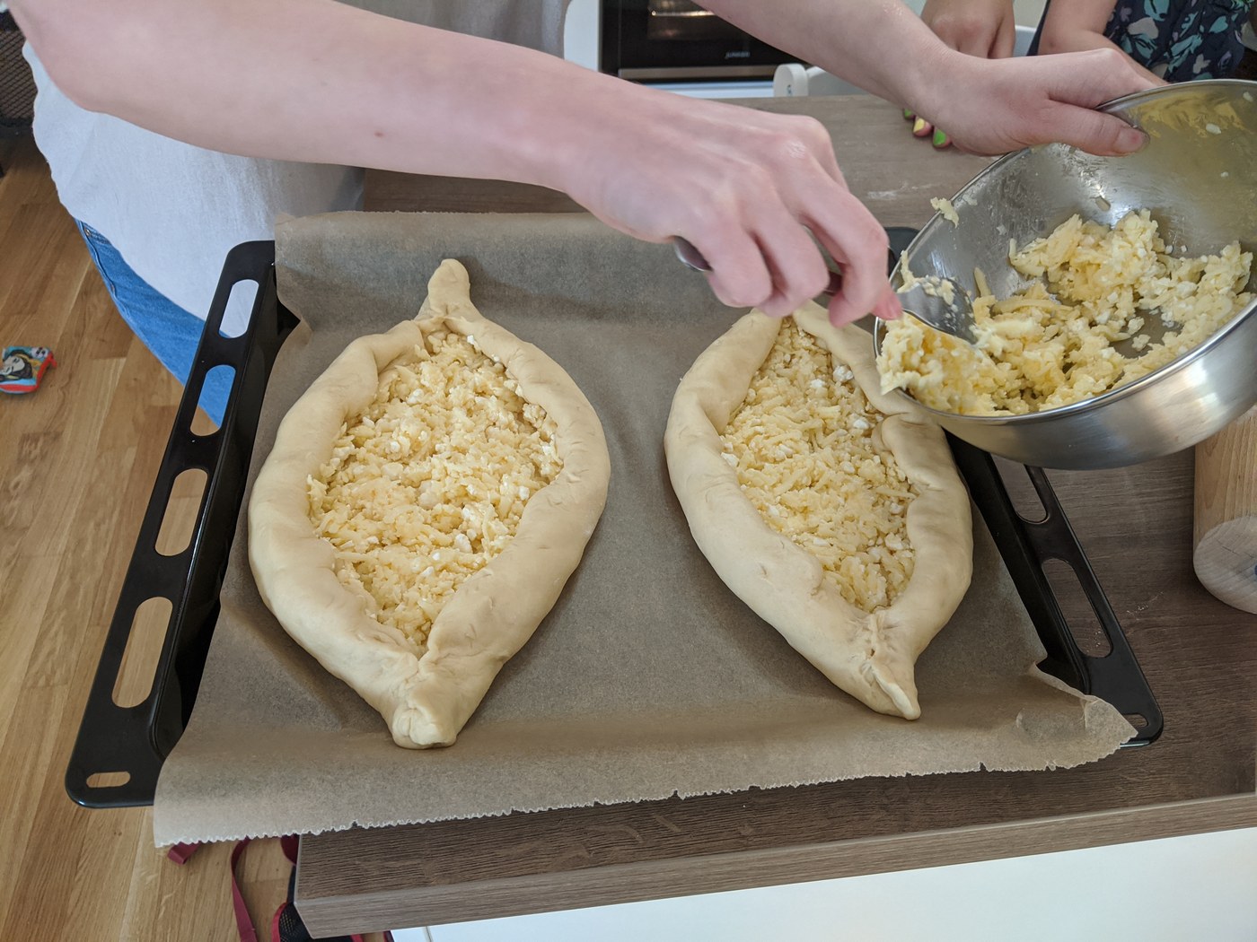 Hands filling boat-shaped Adjarian khachapuri dough with cheese