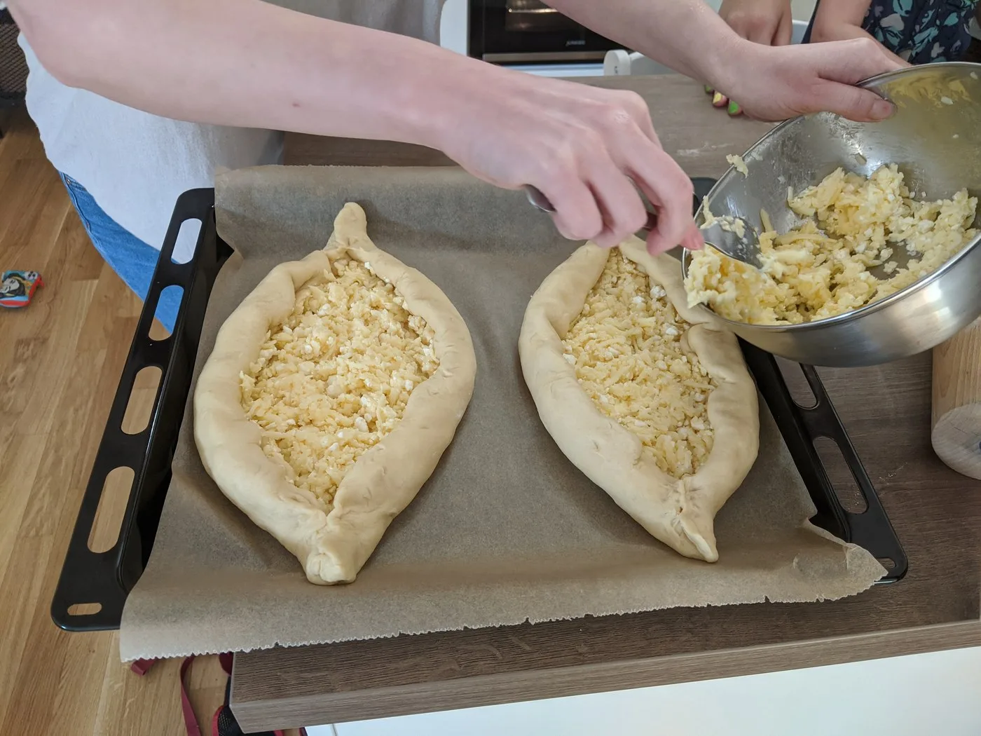 Hands filling boat-shaped Adjarian khachapuri dough with cheese